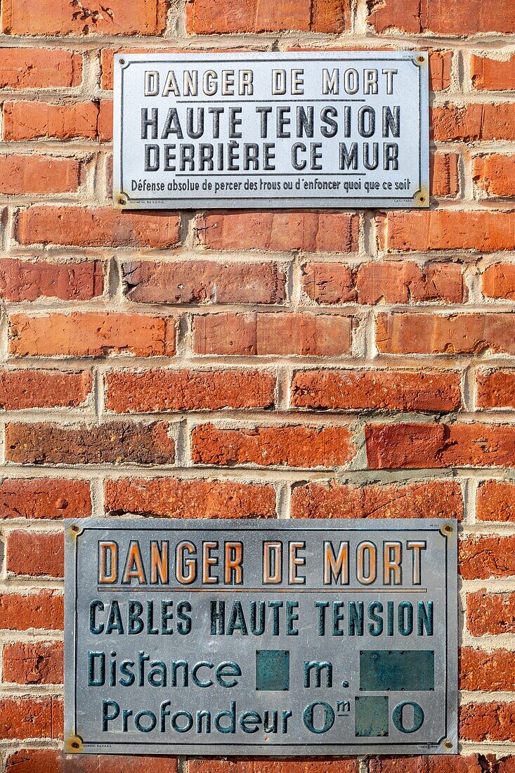 Danger sign, risk of death, high-tension cables behind the brick wall