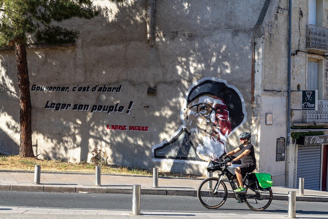Fahrrad vor der Wandmalerei von Murale de abbe pierre, gouverner, c'est d'abord loger son peuple (Regieren heißt, zuerst sein Volk zu beherbergen), rue du faubourg de nimes, montpellier, herault, occitanie, france