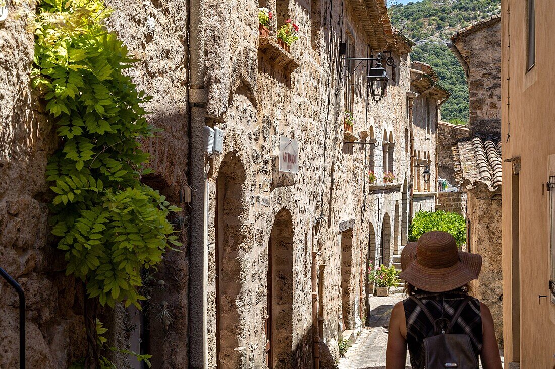 Frau mit Strohhut, kleine Straße in einem der schönsten Dörfer Frankreichs, saint-guilhem-le-desert, herault, okzitanien, frankreich
