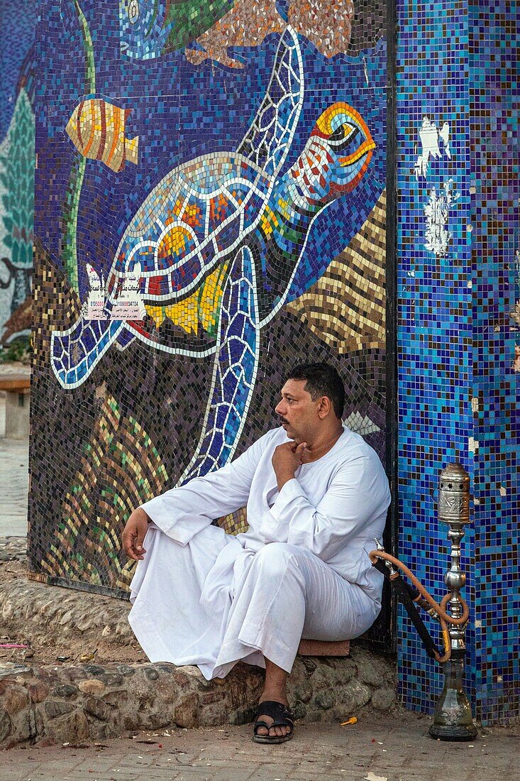 Mann in einer traditionellen Djellaba mit seiner Wasserpfeife, Eingang zum mosaikbedeckten Souk, el dahar Markt, beliebtes Viertel in der Altstadt, hurghada, ägypten, afrika