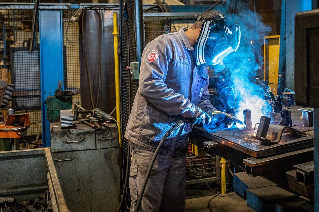 Welding station, welder working on the assembly of metal parts in his factory, l'aigle, orne, normandy, france