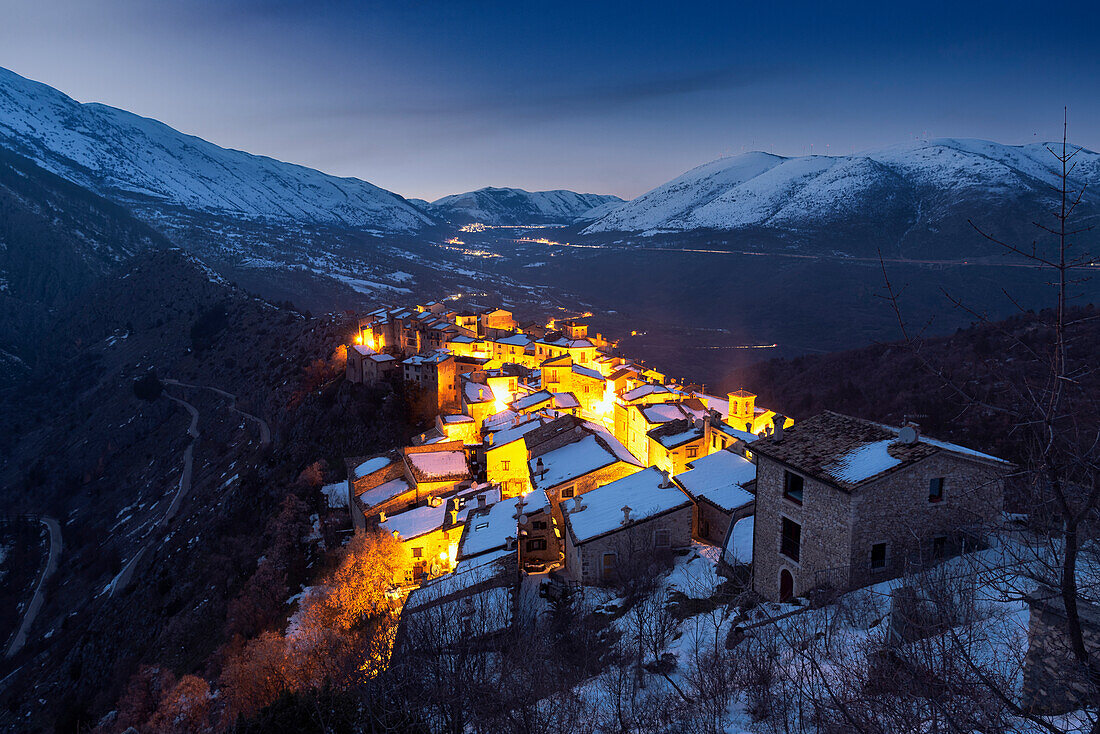 Dusk at the illuminated mountain village of Castrovalva with with snow covered and snowy mountains in the background, L’Aquila province, Abruzzo, Italy