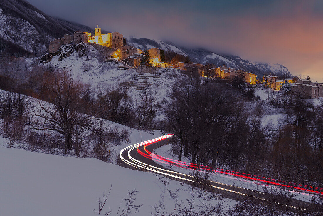 Sunset and car lights on mountain road of illuminated village of Roccacaramanico, Maiella national park, Pescara province, Abruzzo, Italy