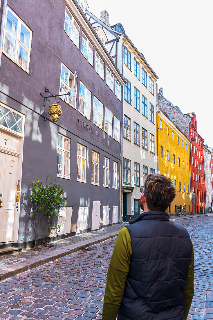 Mann bewundert die Fassaden der bunten Gebäude in der gepflasterten mittelalterlichen Magstraede Straße, Kopenhagen, Hovedstaden Dänemark, Europa