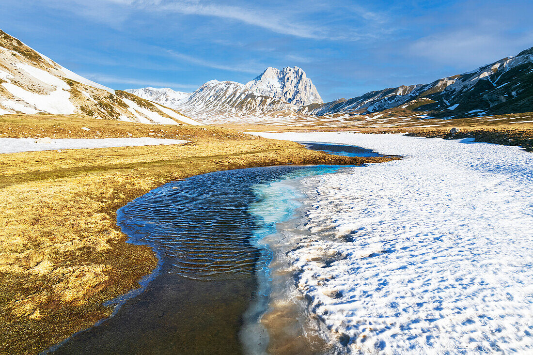 A tiny stream of water making its way during the spring thaw at Campo Imperatore plateau with Gran Sasso peak on the background, Gran Sasso and Monti della Laga national park, L’Aquila province, Abruzzo, Italy