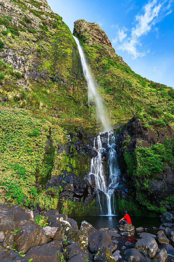 Mann bewundert den Wasserfall von Poco do Bacalhau im Sonnenlicht in Faja Grande, Gemeinde Lajes das Flores, Insel Flores (Ilha das Flores), Azoren-Archipel, Portugal, Europa