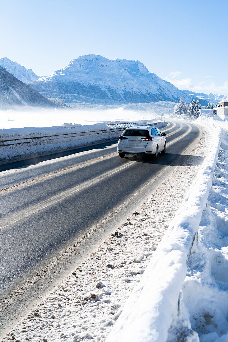 Auto auf vereister Straße in Richtung St. Moritz und schneebedeckte Berge im Winter, Bever, Kanton Graubünden, Schweiz