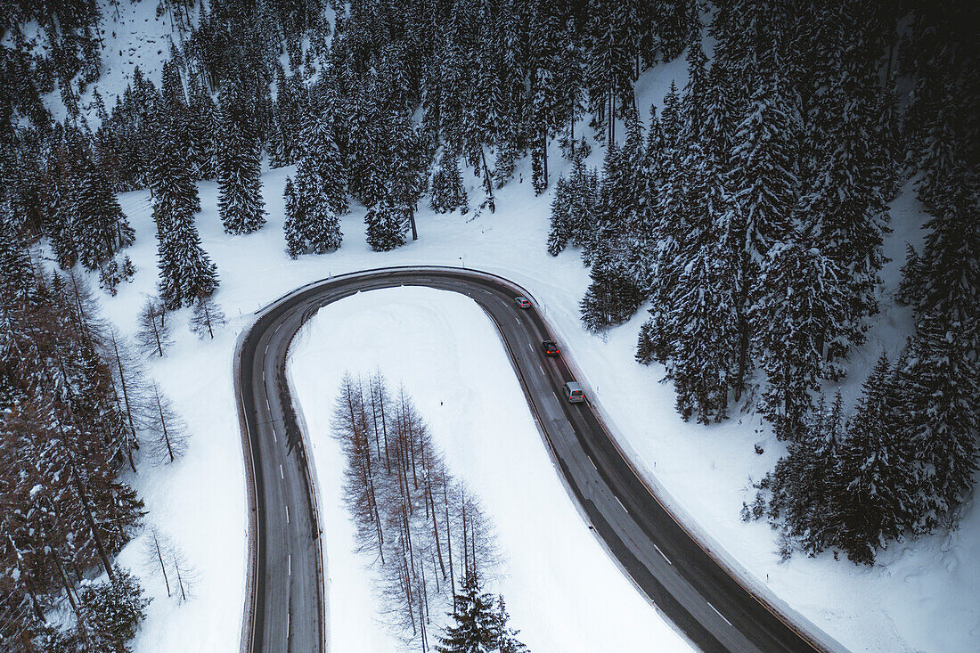 Cars driving on mountain road crossing the winter forest covered with snow