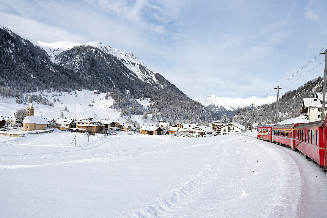 Bernina Express Zug bei der Durchfahrt durch das verschneite Alpendorf Preda Bergun, Albulatal, Kanton Graubünden, Schweiz