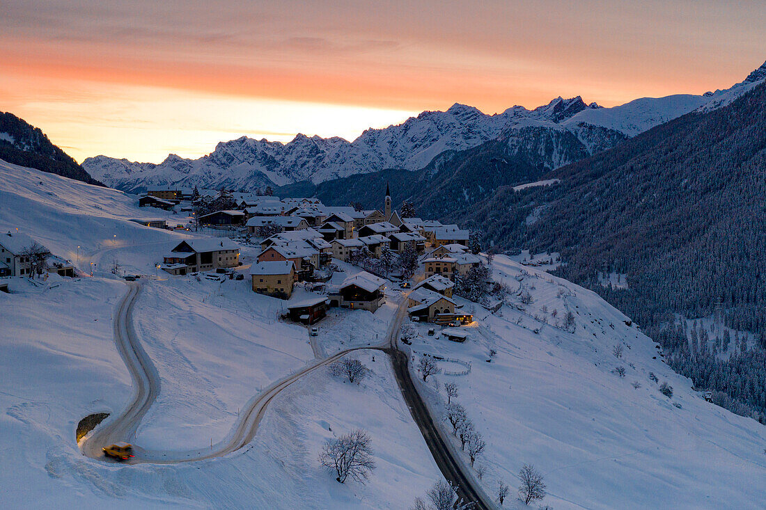 Car on snowy mountain road approaching the alpine village of Guarda at sunrise, Graubunden canton, Engadin, Switzerland