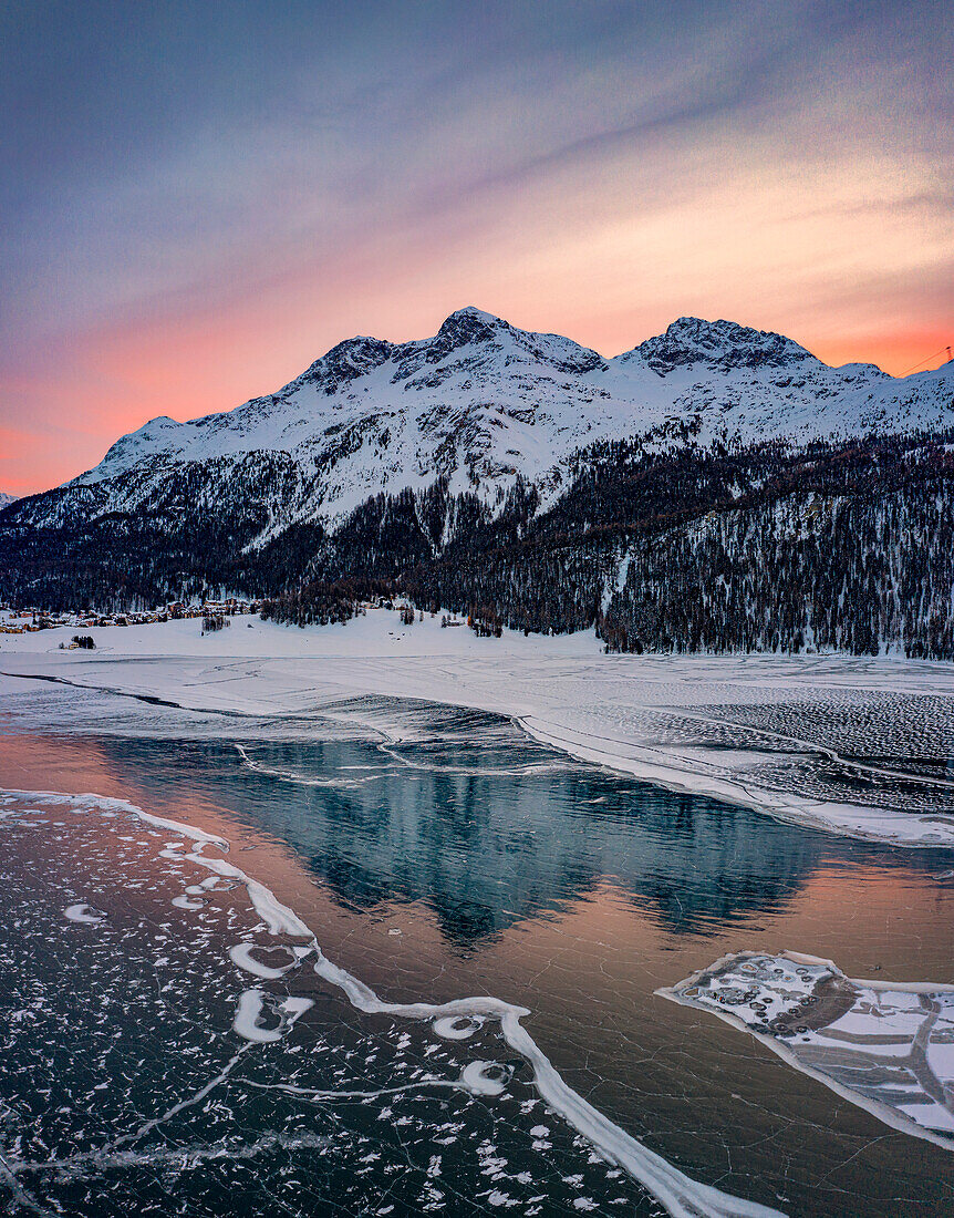 Winterlicher Sonnenaufgang auf schneebedeckten Bergen, die sich im gefrorenen Silvaplanasee spiegeln, Maloja, Engadin, Kanton Graubünden, Schweiz