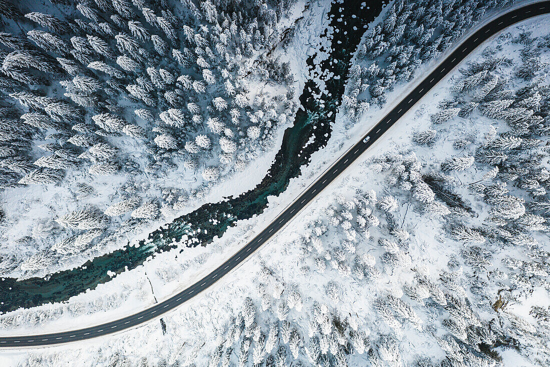 Auto fährt auf verschneiter Bergstraße über gefrorenen Fluss und Wald, Luftaufnahme, Schweiz