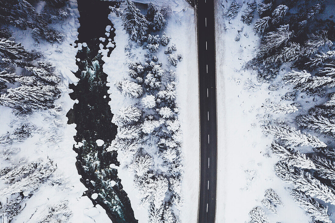 Leere Straße im Schnee, die den gefrorenen Wald und Fluss von oben durchquert, Engadin, Schweiz