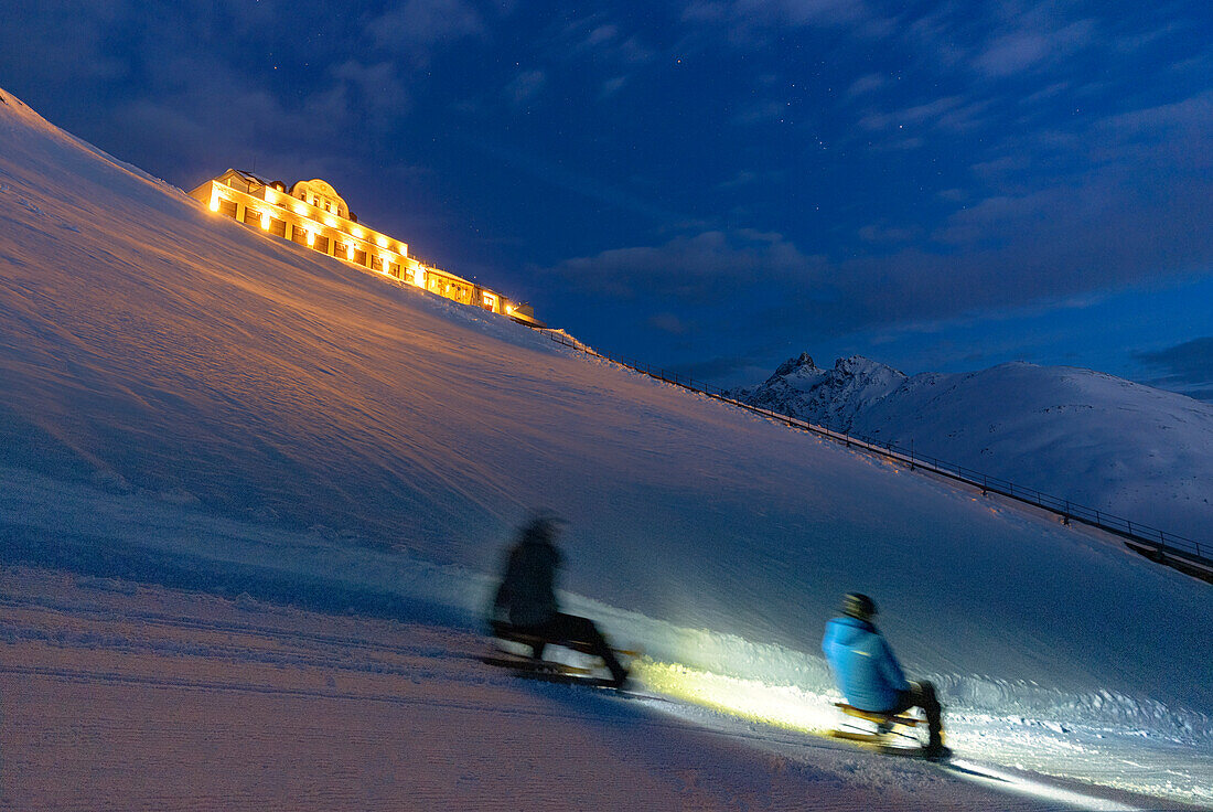 Touristen beim Schlitteln in der verschneiten Landschaft bei Mondschein, Muottas Muragl, St. Moritz, Kanton Graubünden, Engadin, Schweiz