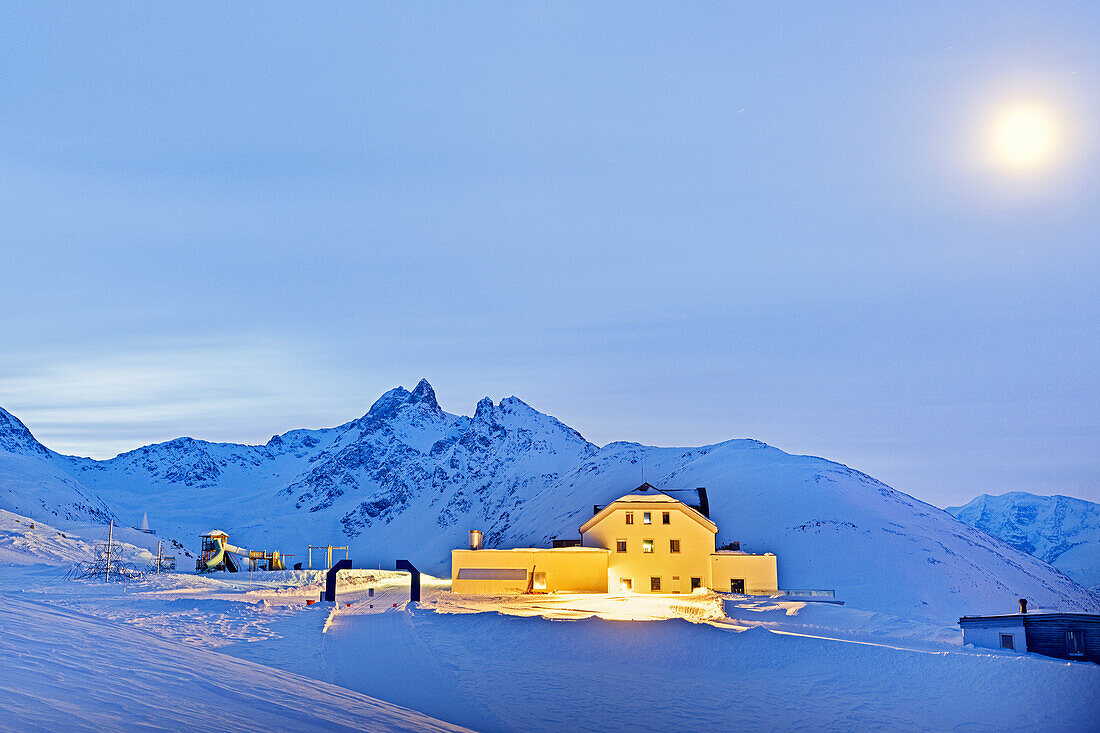 Funicular station and snowy ski slopes lit by moon on a winter night, Muottas Muragl, Graubunden canton, Engadine, Switzerland