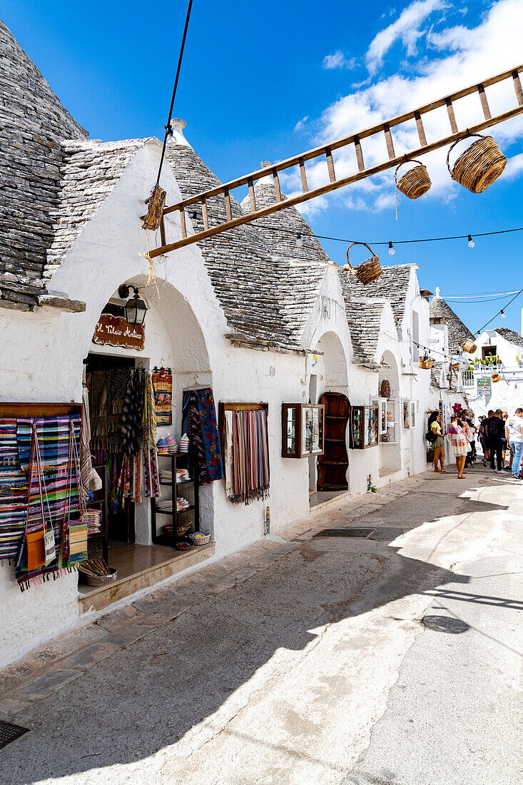 Tourists looking at souvenirs and Trulli huts in the old alley of Alberobello, province of Bari, Apulia, Italy