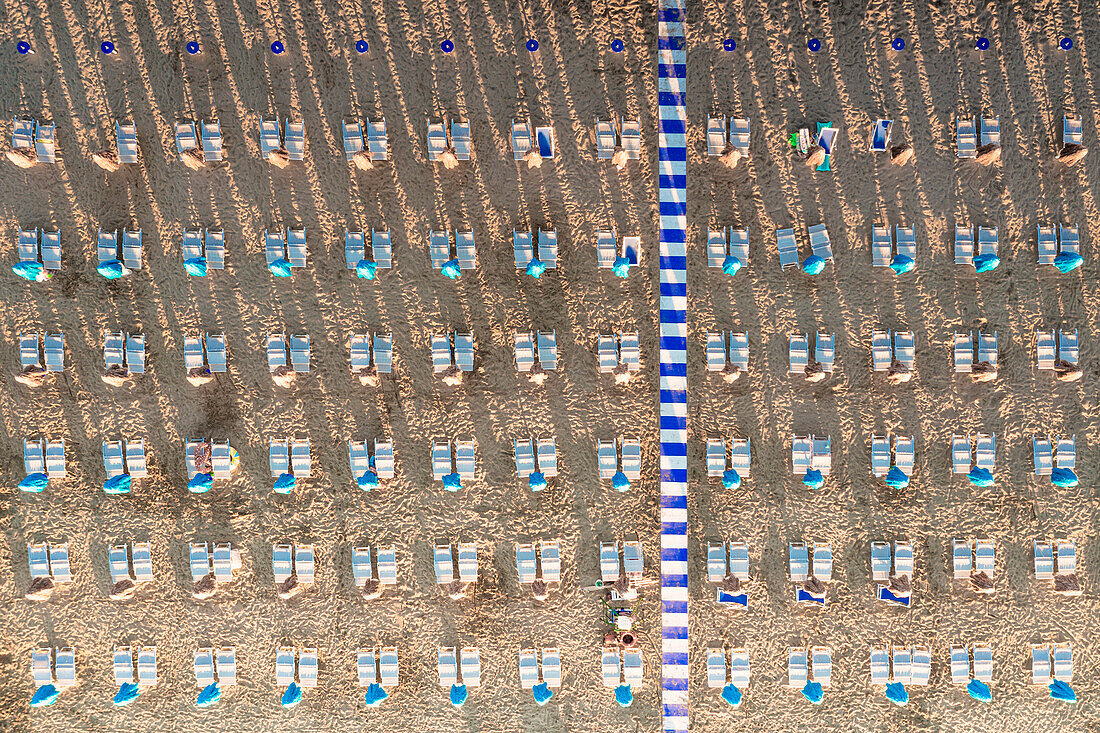 Luftaufnahme von weißen Liegestühlen in einer Reihe am leeren Sandstrand im Sommer, Vieste, Provinz Foggia, Gargano, Apulien, Italien