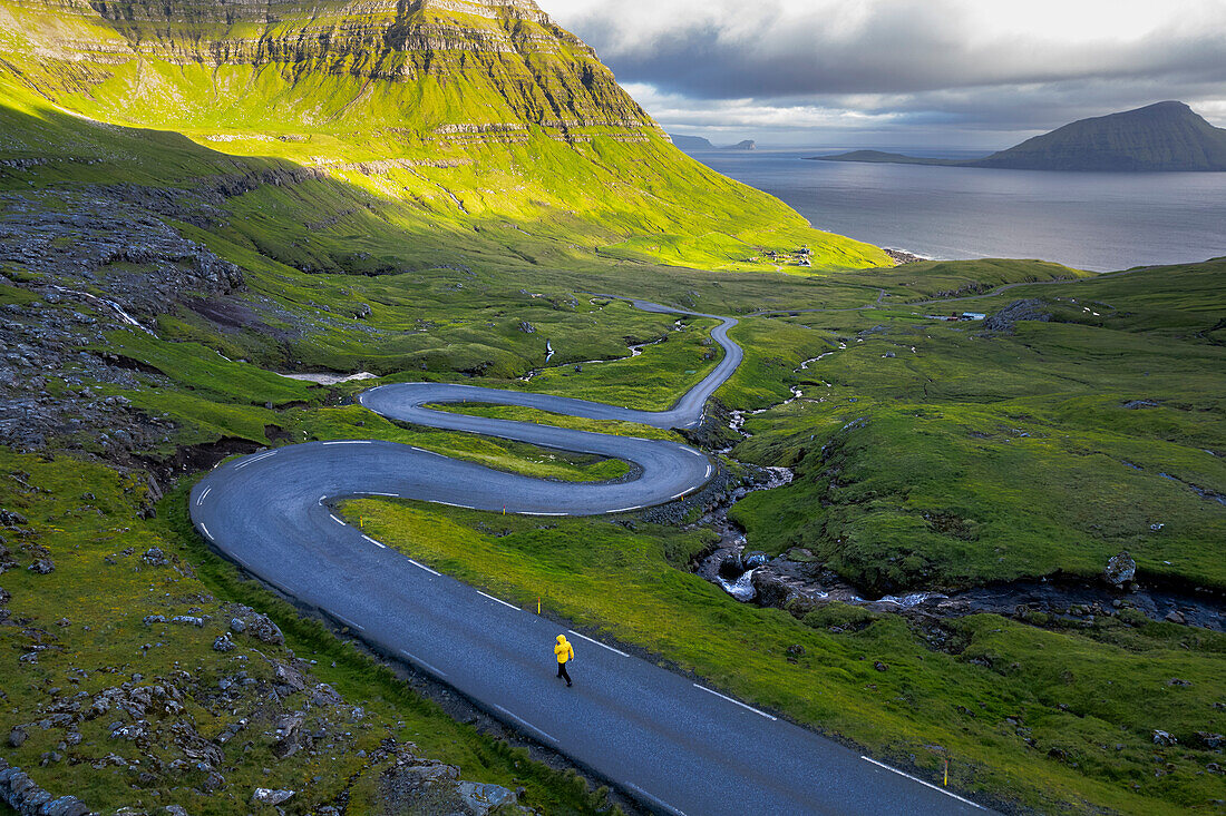 Aerial view of a hiker walking the narrow road with harpin bends of Streymoy island, Faroe islands, Denmark, Europe