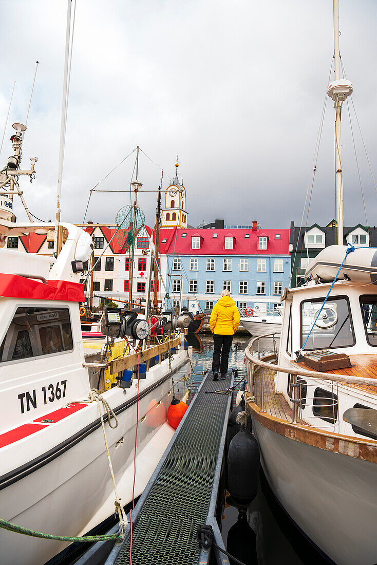Tourist in front of historicals building stands on the pier among boats in the harbour of Torshavn, Streymoy island, Faroe islands, Denmark, Europe
