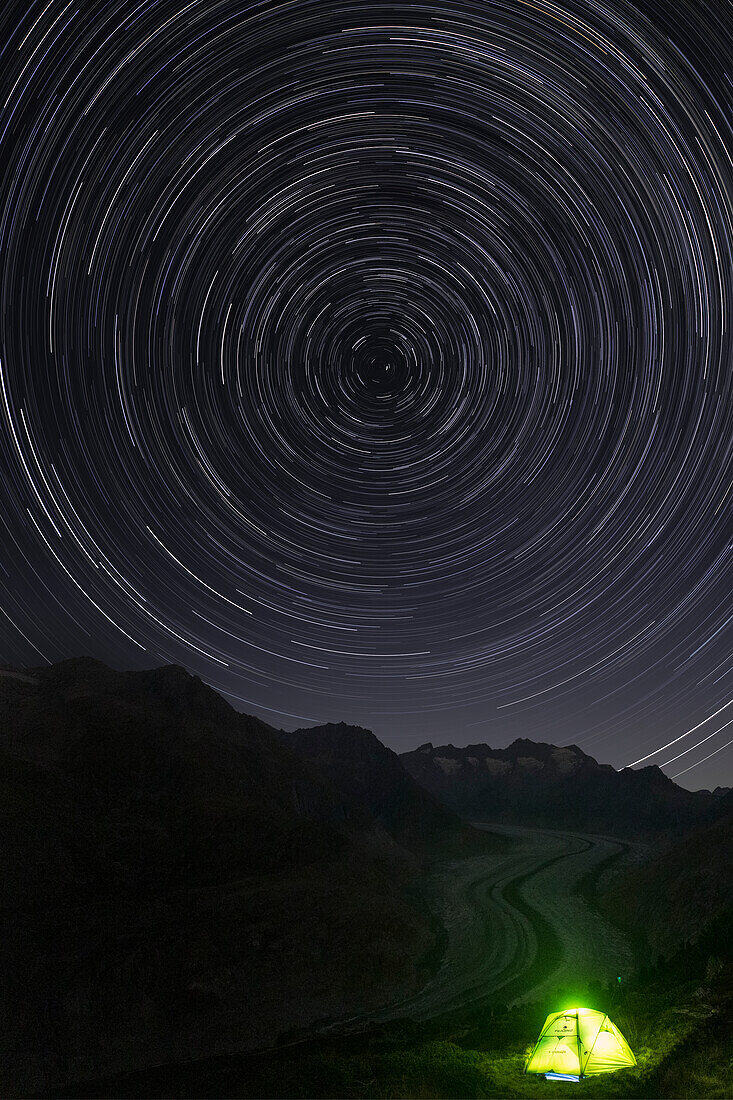 Sternenschweifkreis am Nachthimmel über dem Aletschgletscher und beleuchtetes Zelt auf der Hohfluh Riederalp, Kanton Wallis, Schweiz