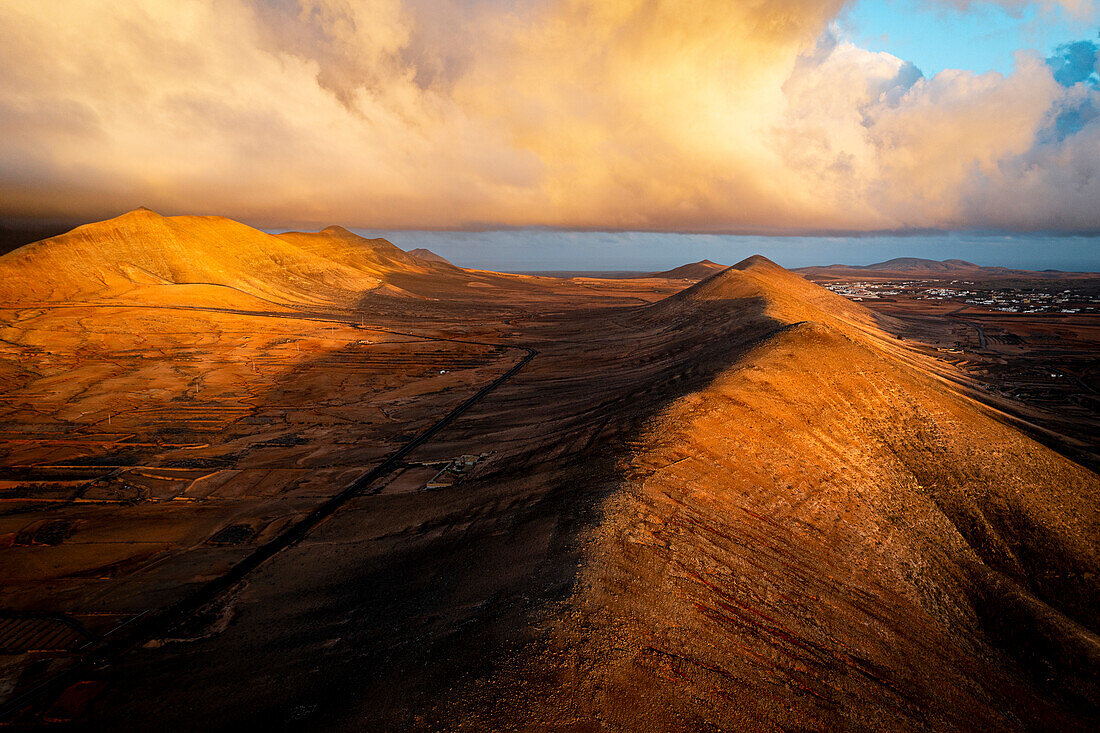 Red volcanic mountains crossed by a straight empty road, Caldereta, Vallebron, Fuerteventura, Canary Islands, Spain