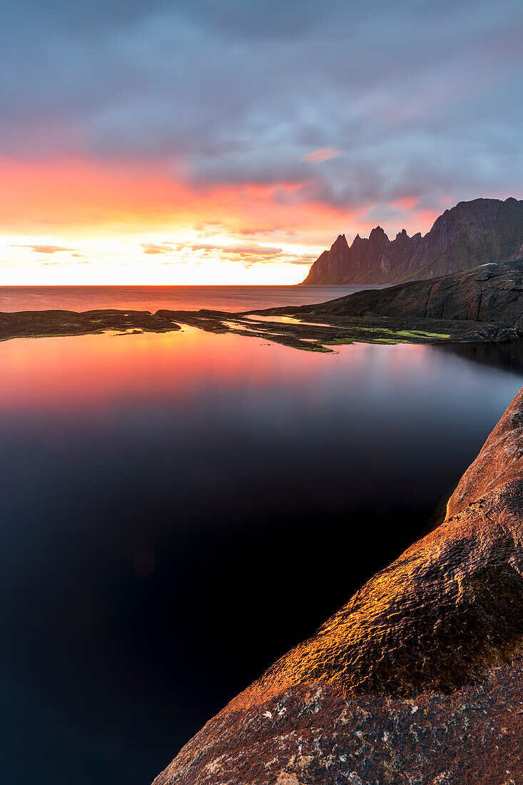 Mitternachtssonne entlang des Fjords und scharfe Bergspitzen, bekannt als Teufelszähne, Tungeneset, Senja, Provinz Troms, Norwegen