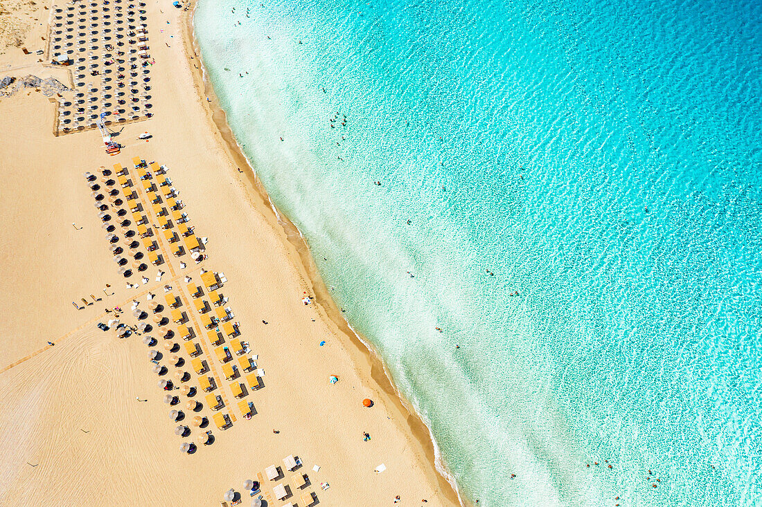 Beach umbrellas and sunbeds on white sand of Falassarna beach overlooking the crystal sea, aerial view, Crete island, Greece
