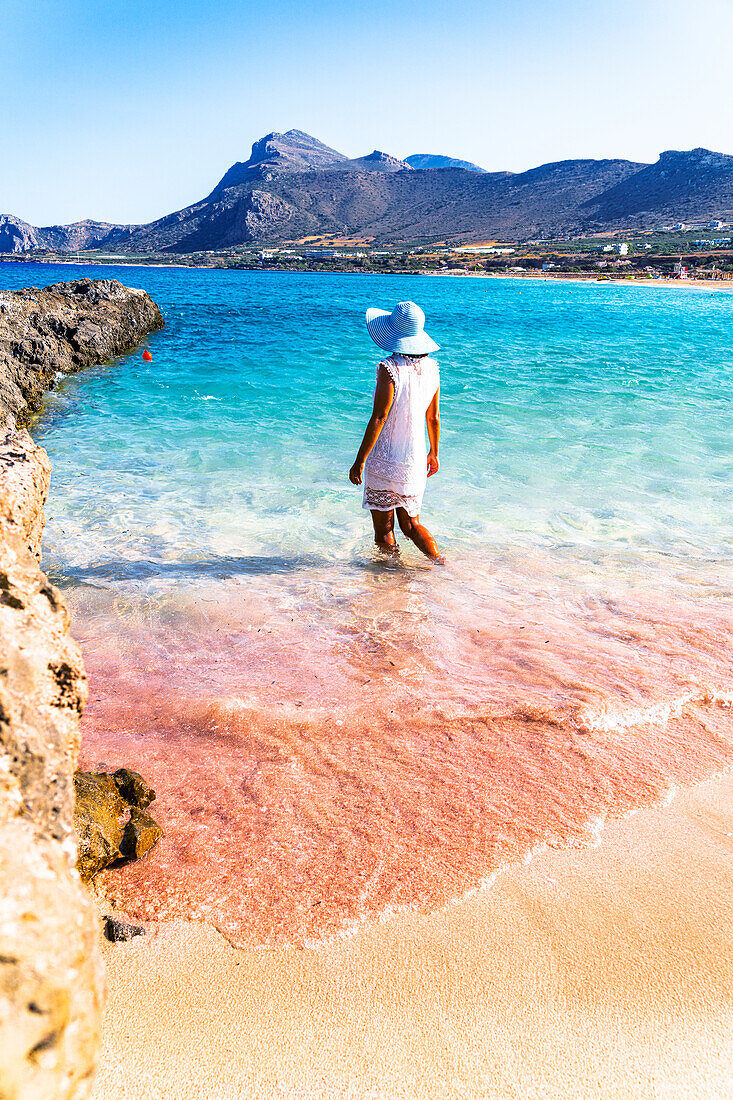 Frau genießt das türkisfarbene Meer am rosafarbenen Sandstrand von Falassarna, Insel Kreta, Griechenland