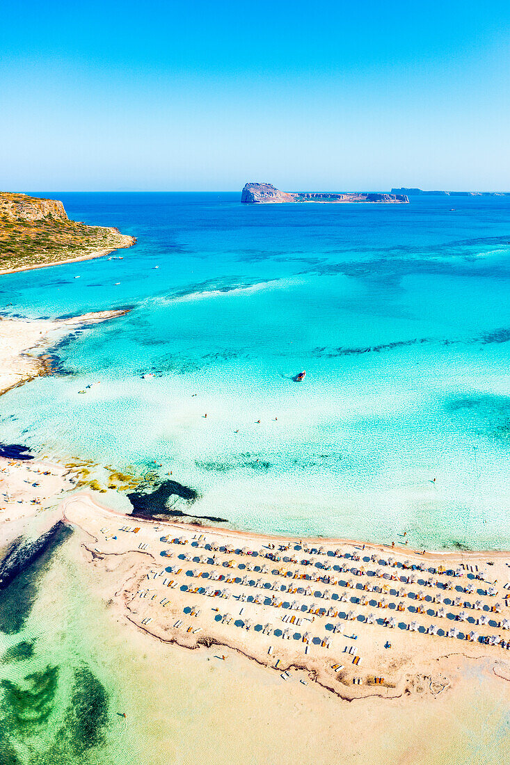 Luftaufnahme von Sonnenschirmen und Liegestühlen am ausgestatteten Strand zwischen Meer und Lagune, Balos, Kreta, Griechenland