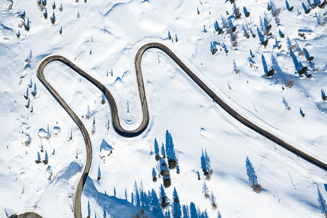 Haarnadelkurven einer verschneiten Bergstraße in der Winterlandschaft, Luftaufnahme, Dolomiten, Italien
