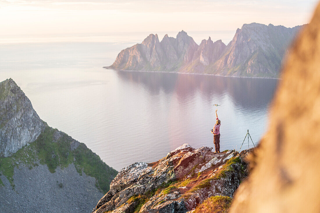 Fotograf auf Berggipfel, der eine fliegende Drohne beobachtet, Insel Senja, Provinz Troms, Norwegen