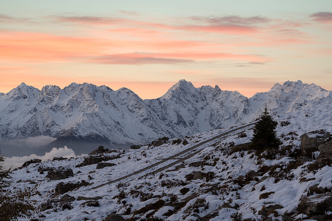 Romantischer rosa Himmel in der Morgendämmerung über der Alpe Rogneda und dem schneebedeckten Pizzo di Coca, Rätische Alpen, Lombardei, Italien