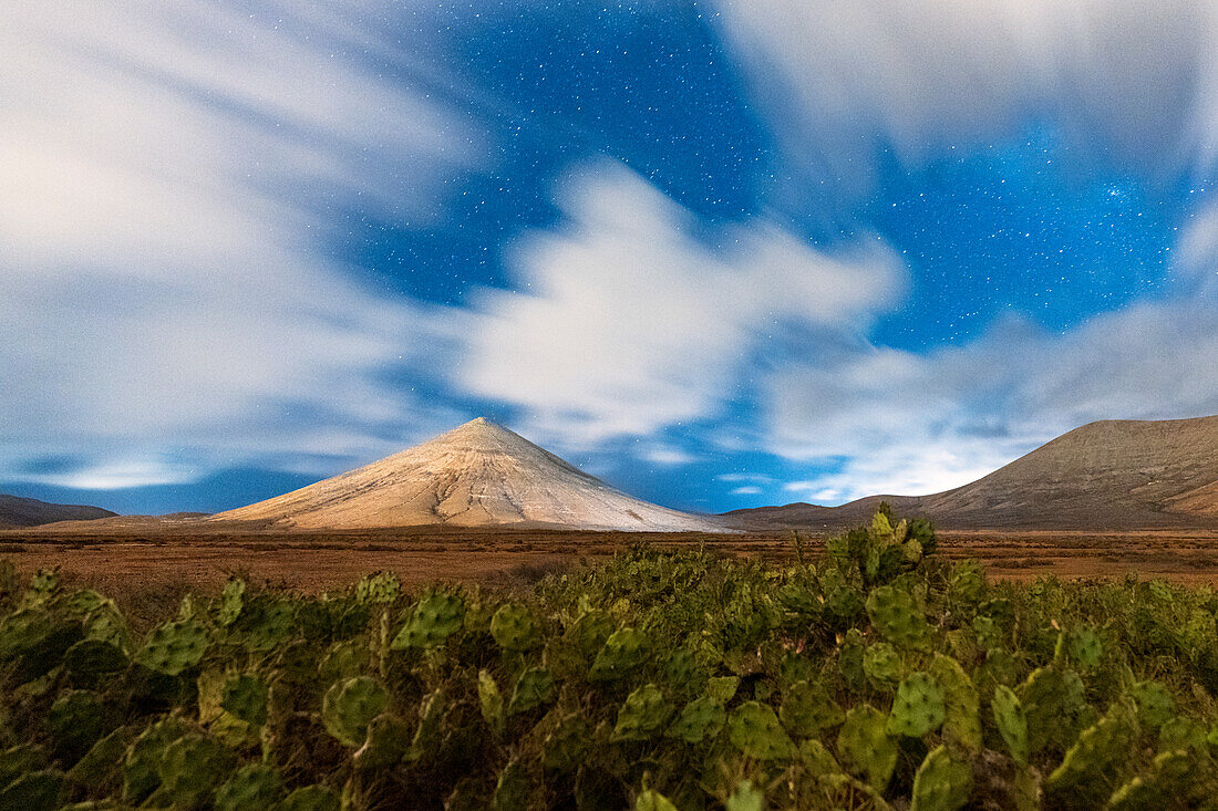 Montana del Fronton und Kakteen unter den Wolken des nächtlichen Sternenhimmels, La Oliva, Fuerteventura, Kanarische Inseln, Spanien