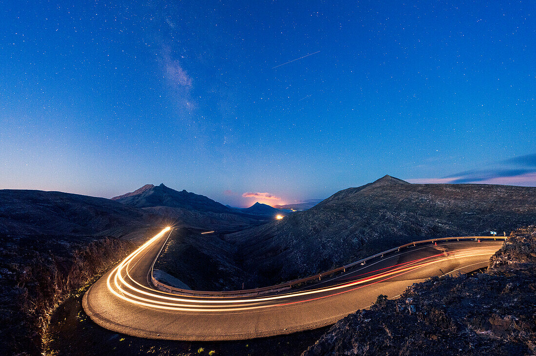 Dämmerung über der Lichtspur eines Autos auf einer leeren Bergstraße, Fuerteventura, Kanarische Inseln, Spanien