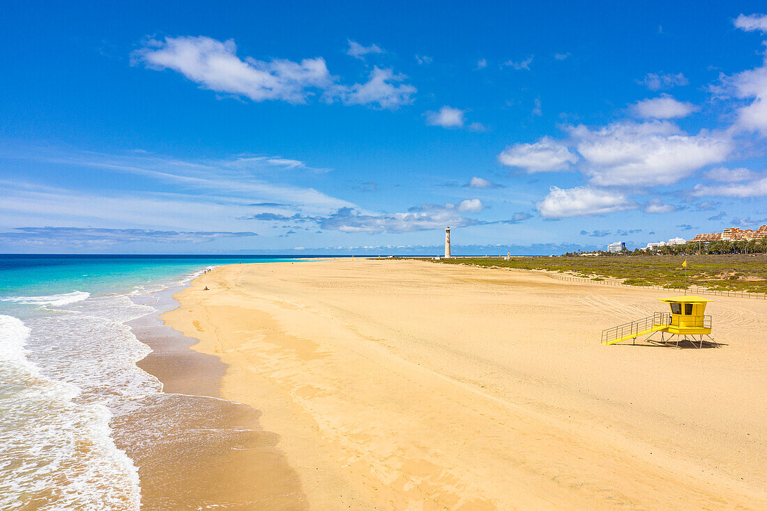 Lifeguard's cabin on empty beach with lighthouse of Morro Jable on background, Fuerteventura, Canary Islands, Spain