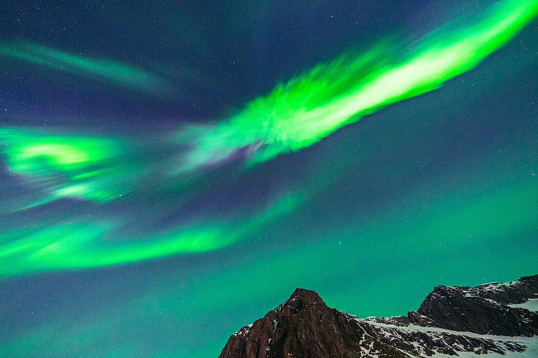 Von hellen Nordlichtern erleuchtete Bergspitze am Nachthimmel, Lofoten, Norwegen