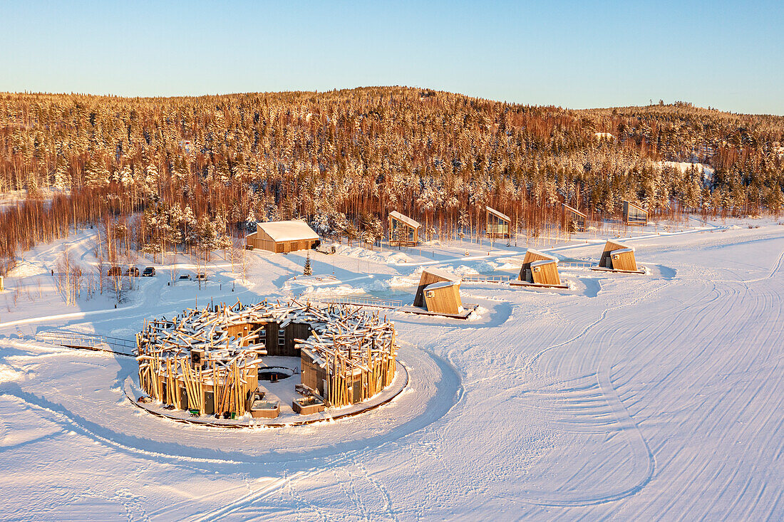 Aerial view of the floating circular building and wood cabins of Arctic Bath Hotel in winter snow, Harads, Lapland, Sweden
