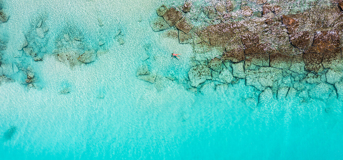 Luftaufnahme einer Frau, die sich auf dem kristallklaren Wasser des Karibischen Meeres treiben lässt, Antigua, Leeward Islands, Westindische Inseln
