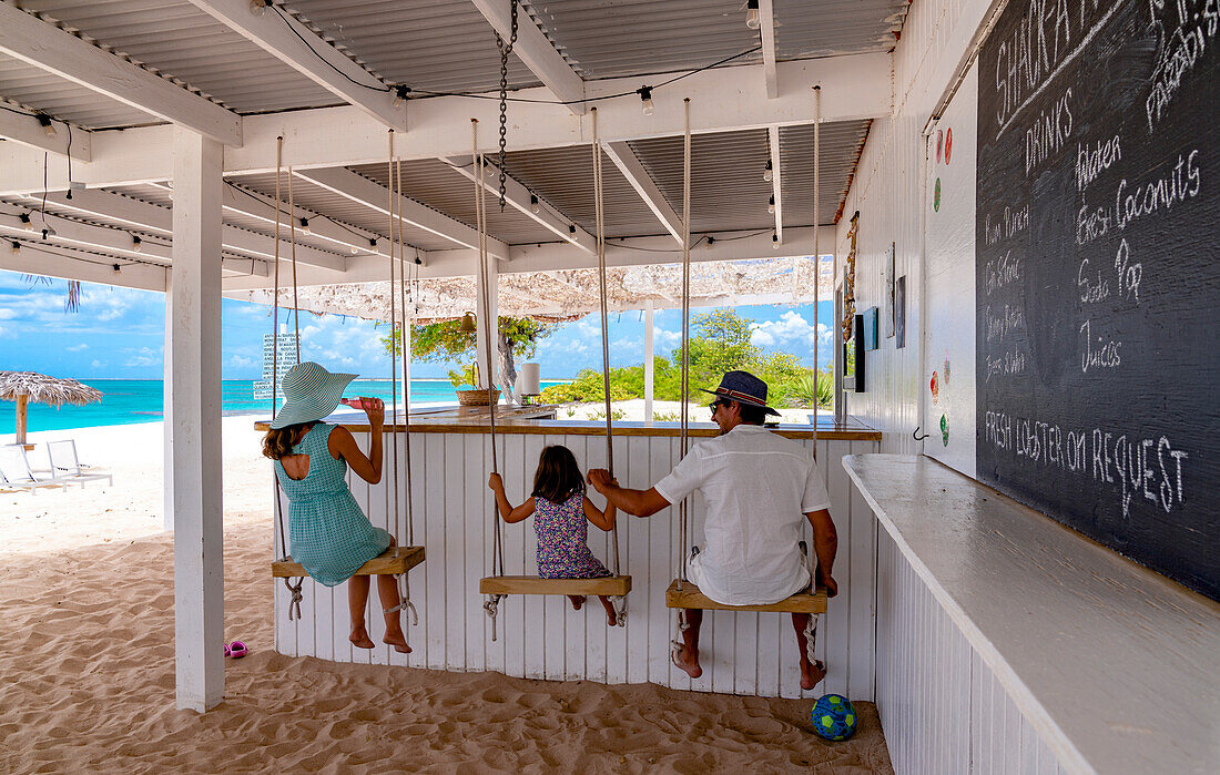 Family with cute little girl playing on swings in a beach bar by the crystal sea, Barbuda, Antigua & Barbuda, Caribbean