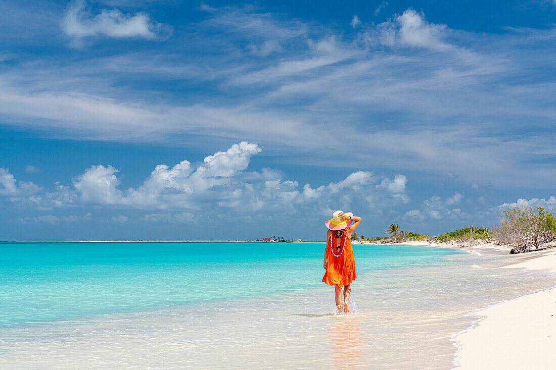 Frau mit Sonnenhut spaziert über einen weißen Sandstrand, der von Wellen umspült wird, Barbuda, Antigua & Barbuda, Karibik, Westindien