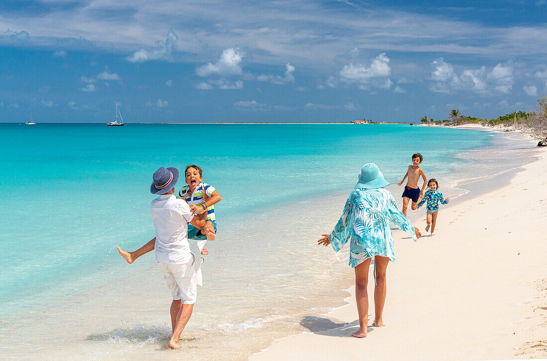 Niedliche kleine Geschwister, die am Strand in die Arme ihres Vaters laufen und springen, Antigua und Barbuda, Karibik, Westindische Inseln