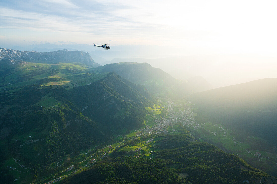 Hubschrauberflug in den nebligen Himmel bei Sonnenuntergang über dem Grödnertal im Frühling, Luftaufnahme, Dolomiten, Südtirol, Italien