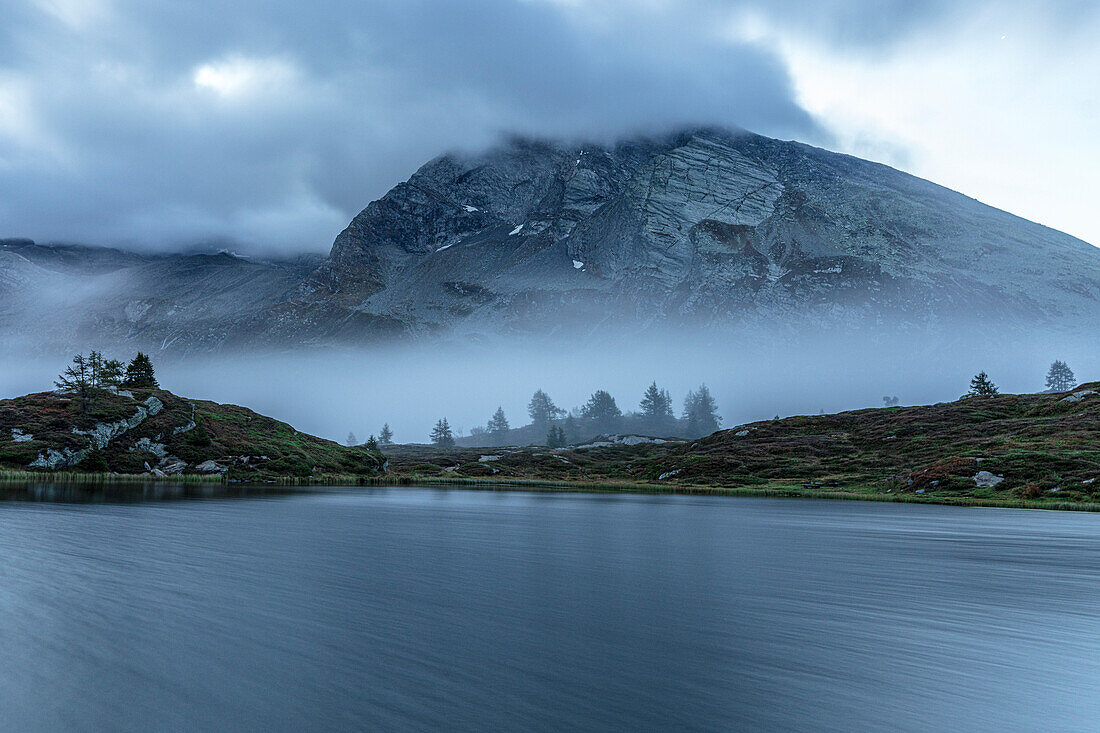 Autumn dusk over Hopschusee lake and Hubschhorn mountain emerging from fog, Simplon Pass, Valais canton, Switzerland