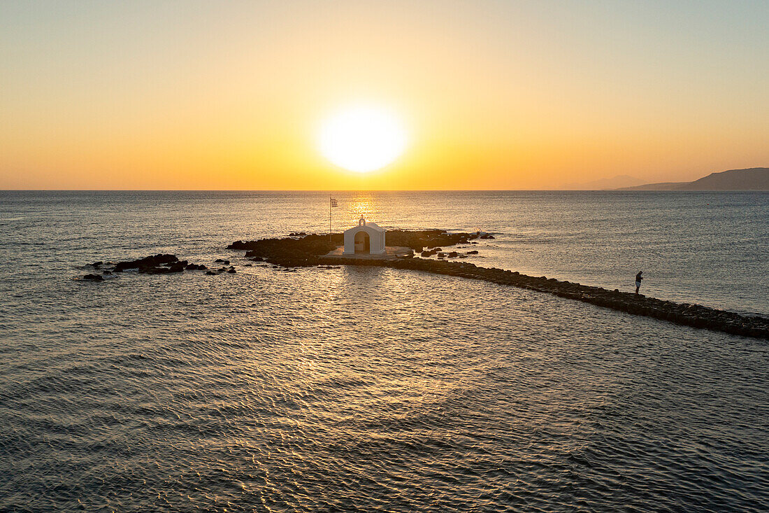 Luftaufnahme einer Person auf dem Pier, die die griechische Kirche und das Meer bei Sonnenaufgang bewundert, Georgioupolis, Insel Kreta, Griechenland