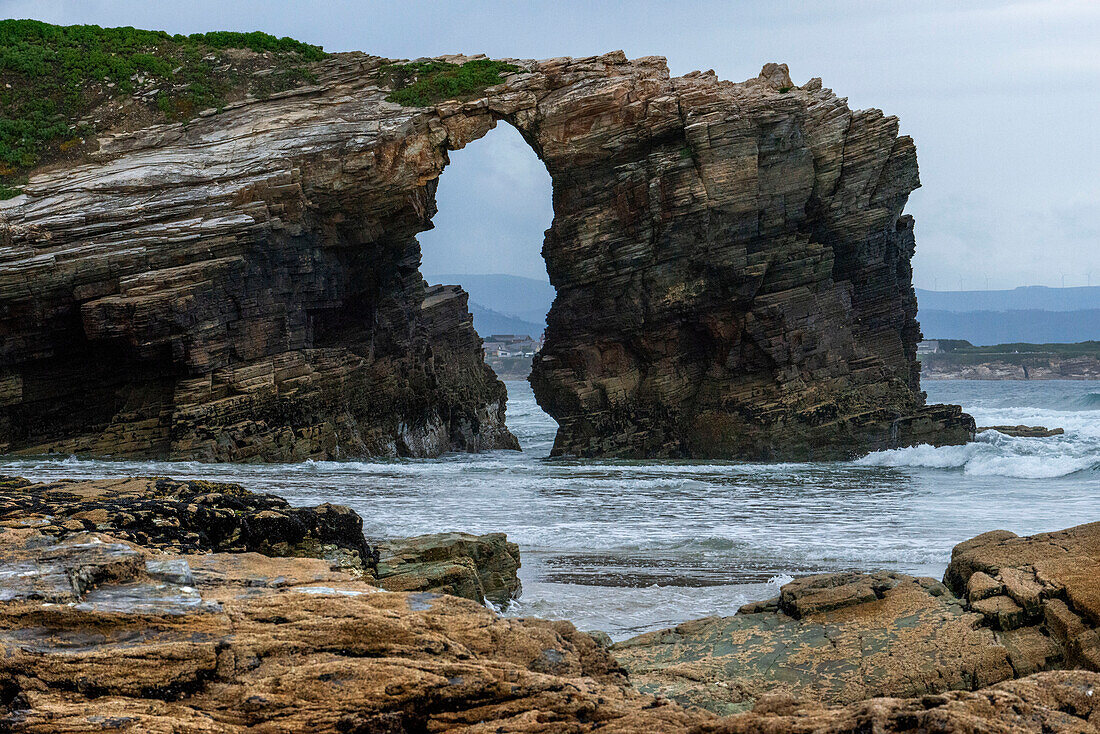 As Catedrais or Las Catedrales Beach by sunset, in Ribadeo, Lugo. Galicia, Spain. Tourists by a stone arch at Beach of the Cathedrals Natural Monument at Ribadeo municipality, Lugo province, Galicia, Spain, Europe