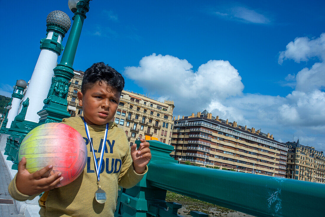 Immigrant boy with a ball in Zurriola bridge, Urumea river and Kursaal in blue hour, Donostia San Sebastián, Basque Country