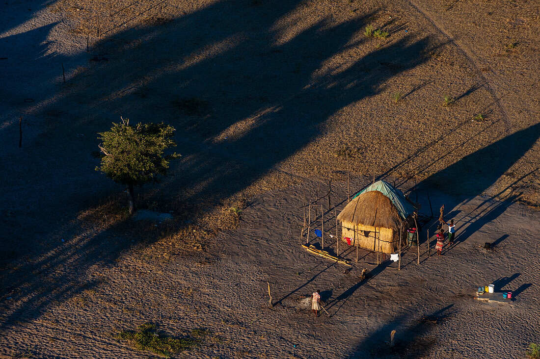 An aerial view of a traditional house with a thatched roof. People working in the yard. Maun, Okavango Delta, Botswana.