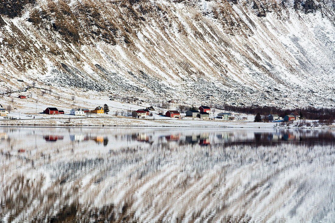 Ein Berg und Häuser spiegeln sich im ruhigen Wasser eines Sees. Eggum, Lofoten-Inseln, Nordland, Norwegen.