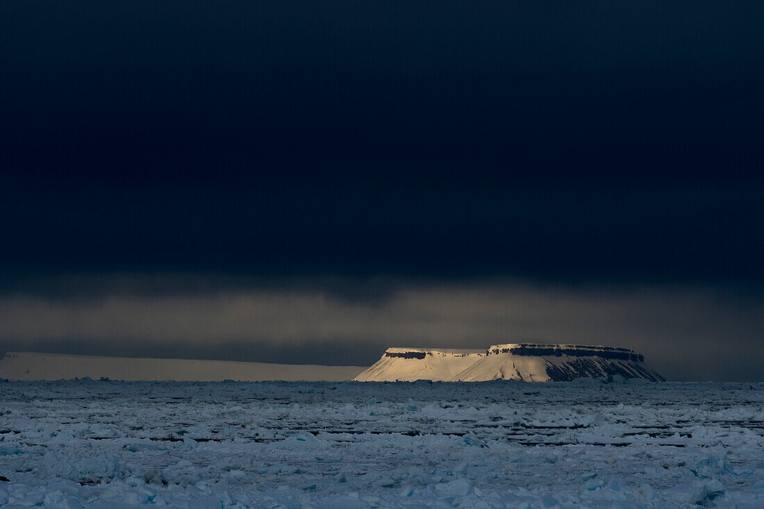 A sunlit mountain emerges from the sea ice in the Erik Eriksenstretet. Nordaustlandet, Svalbard, Norway.