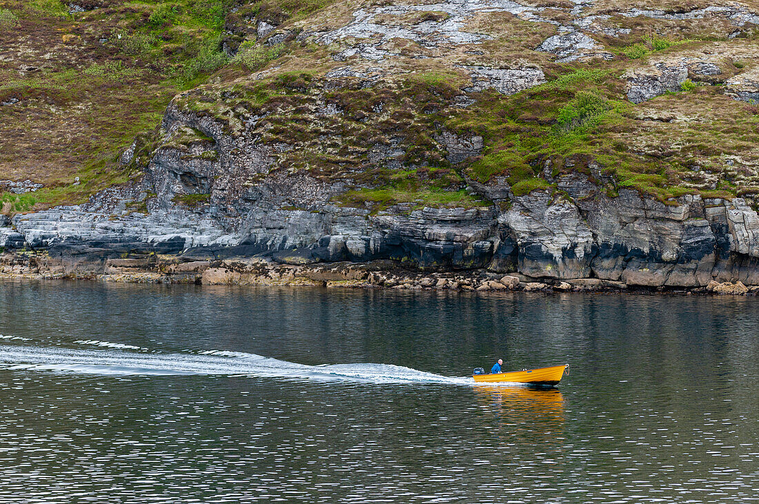 Ein kleines Motorboot hinterlässt eine Spur, während es auf dem Svesfjord an Bergen vorbeifährt. Svesfjorden, Sor Throndelag, Norwegen.